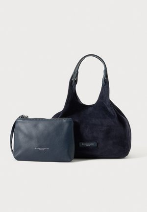 Bolso de mano de ante azul marino con asa sencilla junto a un estuche pequeño de cuero con cremallera, ambos con etiqueta Gianni Chiarini Firenze.