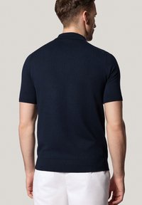 Granatowa koszulka polo z krótkim rękawem, wykonana z miękkiego dzianinowego materiału, z klasycznym kołnierzykiem i ściągaczami przy rękawach, o dopasowanym kroju.