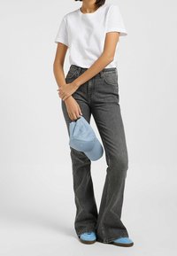Jeans grises de campana con una cintura alta, combinados con una camiseta blanca, sosteniendo una gorra azul clara. Unos zapatos azules con una suela marrón completan el atuendo.