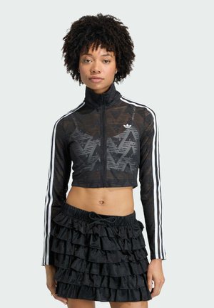 Black cropped jacket with geometric pattern, zip closure, and white stripe accents. Paired with a black ruffled skirt.