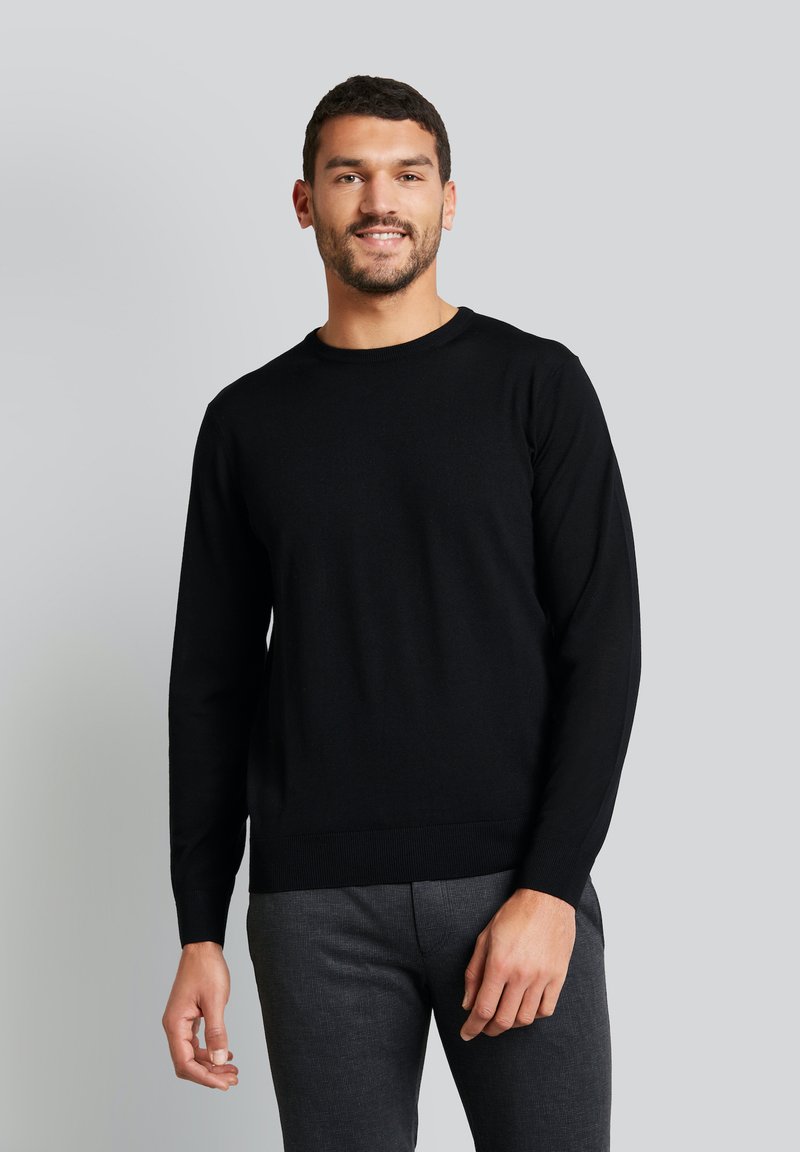 Schwarzer Strickpullover mit langen Ärmeln und Rundhalsausschnitt, mit einer glatten Textur und gerippten Bündchen, kombiniert mit dunkelgrauen, taillierten Hosen.