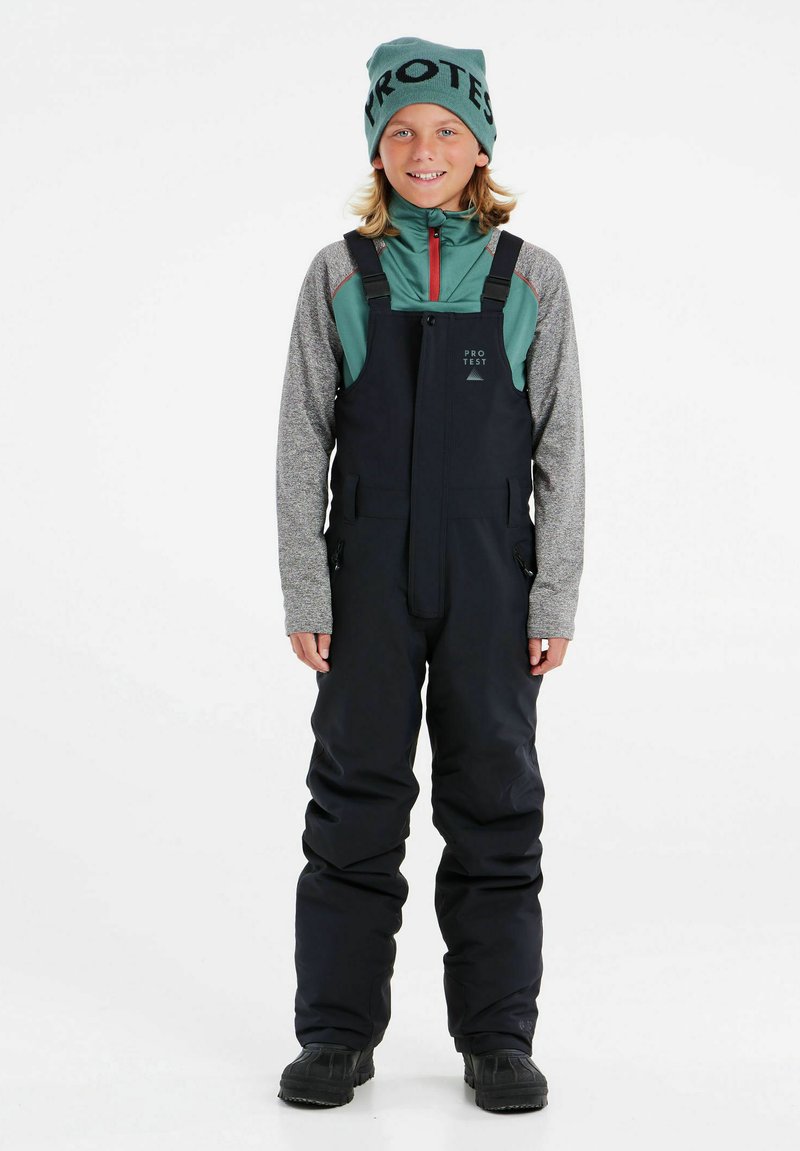 Zwarte sneeuwoverall met verstelbare bandjes, ritszakken en een waterdicht ontwerp, gecombineerd met een teal en grijs shirt met lange mouwen en een muts.