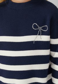 Maglione a righe blu navy e bianco in maglia, con un dettaglio di fiocco in strass sul petto, collo rotondo e polsini a costine.