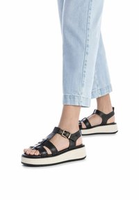 Sandalias de plataforma de cuero negro con hebilla, que presentan un diseño de punta abierta y múltiples correas. Combinadas con unos jeans cortos de color azul claro.