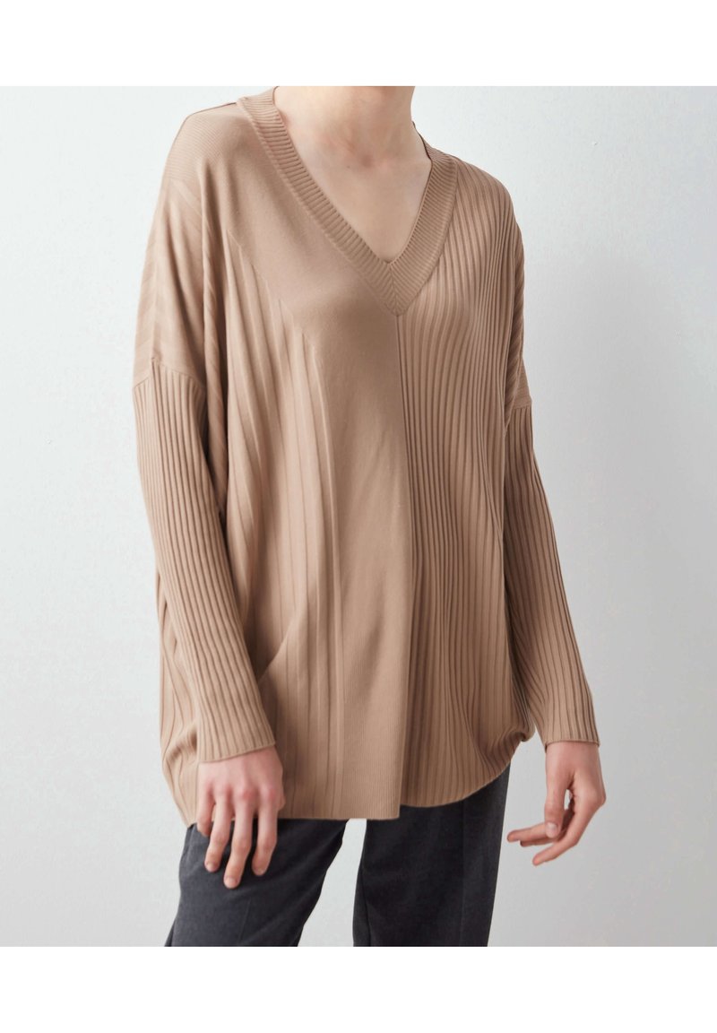 Top beige à rayures côtelées à manches longues avec un col en V, présentant une coupe décontractée et des épaules baissées. Texture douce, design subtil et manches de longueur mi-longue.