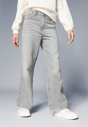 Hellgraue weit geschnittene Jeans mit hoher Taille, Fünf-Taschen-Design und dezenten Nähten, kombiniert mit weißen Sneakers.