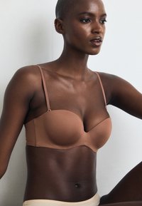 Soutien-gorge avec des bonnets lisses et moulés dans une teinte brun clair, doté de fines bretelles et d'un design sans couture. Convient à diverses tenues.