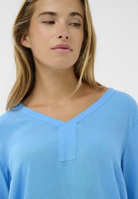 Haut bleu clair à encolure en V, fabriqué dans un tissu doux et texturé, avec un détail discret de couture avant et une coupe décontractée.