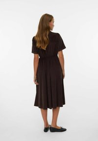Robe marron à manches courtes, avec une coupe décontractée et une taille élastique, arrivant au mi-mollet. Tissu doux avec un léger éclat. Chaussures plates noires.