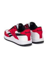 Piros és fehér sportcipők fekete részletekkel, szintetikus bőr felsőrésszel, fűzős kialakítással és lapos gumitalppal. Márkajelzés a saroknál.