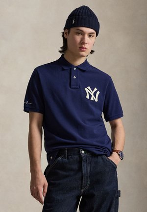 Tengerészkék galléros póló fehér, hímzett 'NY' logóval, rövid ujjú és klasszikus gallérral, sötét farmernadrággal és órával párosítva.