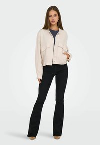 Kort beige jasje met twee voorzakken, knoopsluiting en een geribbelde zoom. Gecombineerd met zwarte uitlopende jeans en een marineblauw top.