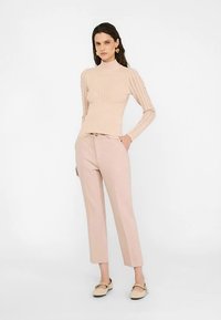 Lichtbeige gebreide trui met een hoge hals en gestructureerde verticale strepen langs de armen. Gecombineerd met lichtroze op maat gemaakte broek.