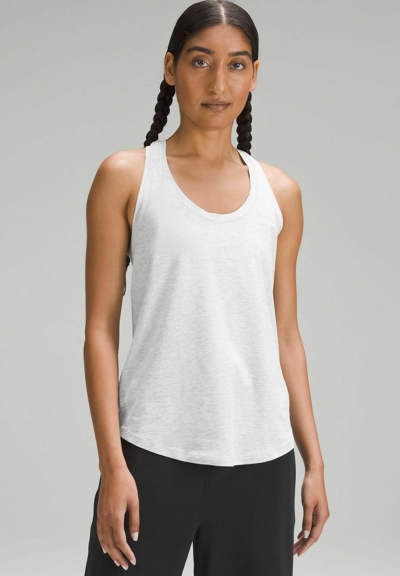 White tank top in a soft, lightweight fabric with a round neckline and a relaxed fit, paired with black pants. Smooth texture, no patterns.