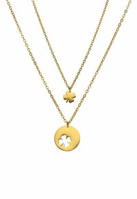 Collier à plusieurs couches en ton doré présentant deux chaînes. L'une a un petit charm en forme de trèfle à quatre feuilles ; l'autre met en avant un pendentif circulaire avec un trèfle découpé.