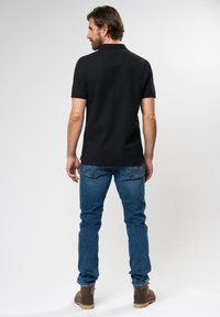 Black polo shirt with short sleeves, collar, and side slits, paired with blue jeans. The outfit is complemented by brown boots.
