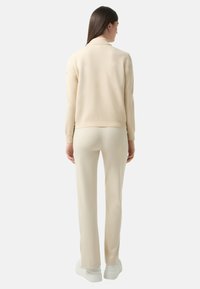 Beżowy sweter robiony na drutach z prążkowanym kołnierzem, zestawiony z dopasowanymi spodniami wąskimi. Gładka tekstura, minimalny design i białe buty na platformie.