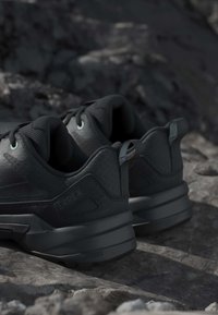 Black hiking shoes with thick soles resting on rocky terrain, designed for outdoor use with padded collars and pull tabs.
