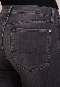 Czarne dżinsy o lekko wyblakłej fakturze, tylna kieszeń z haftem oraz metka z logo blisko pasa.
