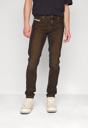 Braune Denim-Jeans mit schmalem Schnitt, ausgestattet mit einer strukturierten Oberfläche, Gürtelschlaufen und Fronttaschen, kombiniert mit weißen High-Top-Sneakern.