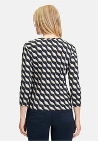 Granatowa bluzka z kremowym falistym wzorem, rękawami 3/4, prążkowaną teksturą, okrągłym dekoltem, w zestawie z ciemnymi spodniami.