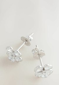 Cercei stud din argint în formă de floare, cu patru petale, fiecare având o piatră clară centrală. Textură metalică netedă cu finisaj reflectorizant.