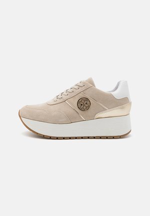 Beige suede sneaker with a white heel, gold accents, round logo on the side, and a thick white platform sole with textured grip.