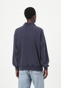 Felpa oversize blu navy dal tessuto morbido, con spalle scese, colletto e polsini a coste, abbinata a jeans chiari.