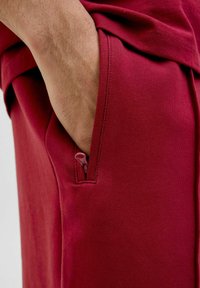 Sweatshirt bordeaux avec une poche zippée, présentant une texture douce et un design ajusté. Vue rapprochée montrant une main dans la poche.
