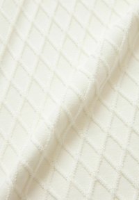 Vävt bomullstyg i off-white med ett texturerat diamantmönster, som har upphöjda gallerliknande detaljer för extra dimension.