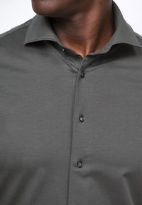 Grijze poloshirt met een klassieke kraag, vijf zwarte knopen en een gladde textuur. De stof lijkt licht van gewicht en zacht te zijn.