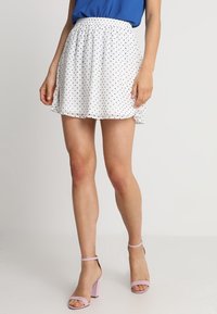 Bílá sukni s puntíky, elastickým pasem, krátká délka a volný design. V kombinaci s levandulovými podpatky.