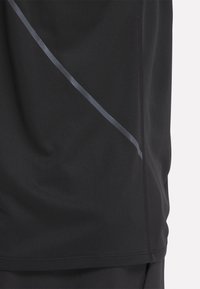Černé sportovní tričko s texturovaným povrchem, se šedým diagonálním pruhem. Design zahrnuje krátké rukávy a kulatý výstřih.