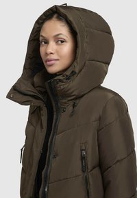Giacca a vento marrone con un ampio cappuccio, zip frontale e coulisse regolabili. Presenta un motivo trapuntato e tasche laterali con zip.