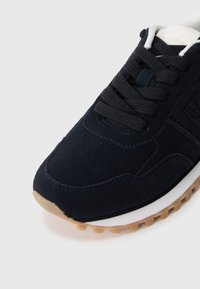 Jūras spēku zila zamšas kedas ar strukturētu virsu, melniem šņorēm, baltu zoli un gumijas ārējo zoli, kurai ir mazi saķeres uzgaļi.