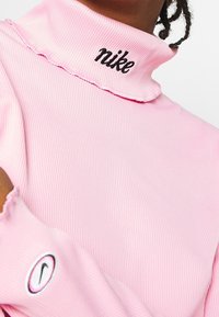 Rosa ribbad polokrage topp med broderad "nike" logotyp vid kragen och en svart konturerad swoosh logotyp på ärmen.