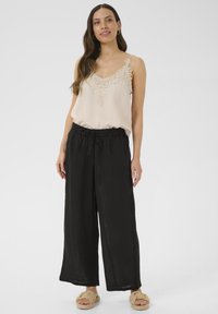 Débardeur beige clair avec des détails en dentelle, associé à un pantalon noir à jambes larges et des sandales tressées beiges, créant une tenue décontractée.