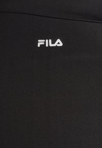 Schwarze sportliche Leggings aus dehnbarem Stoff, mit einer glatten Textur und einem weißen FILA-Logo auf der unteren Vorderseite.