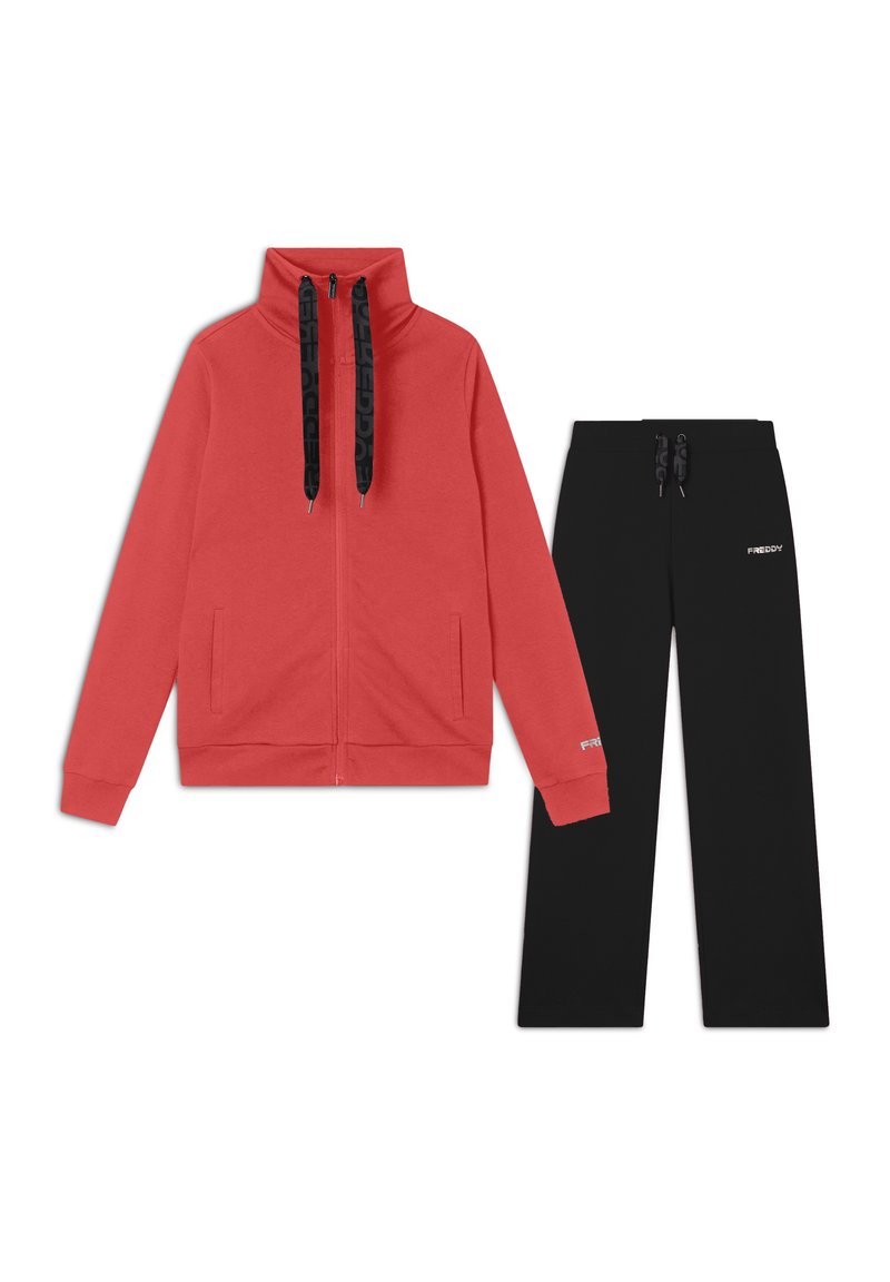 Giacca rossa con zip e colletto alto, abbinata a pantaloni tuta neri con logo e vita elasticizzata.