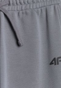 Gros plan d’un tissu gris avec une ceinture élastique et un cordon, avec un logo partiel noir « 4F » sur le côté droit.