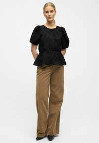 Sort tekstureret peplum-top med puffærmer og blomsterprint, parret med højtaljede brune cordwainnederdele med vidde og sorte høje hæle.