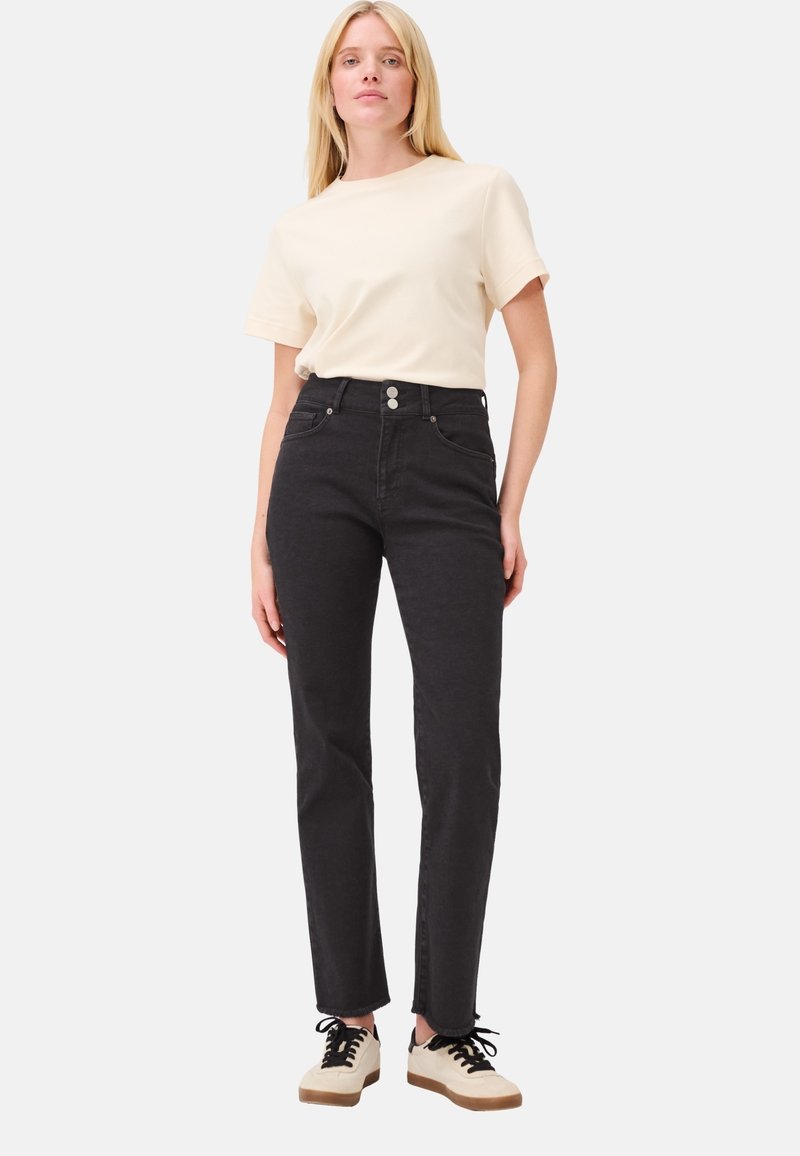 Zwarte hoog gewelfde jeans met een strakke pasvorm, twee voorkeurszakken en een sluiting met twee knopen. Gepaard met een lichtbeige t-shirt met korte mouwen.