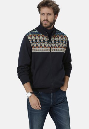Marineblauer Reißverschluss-Pullover mit gemustertem oberen Design in Orange, Blau und Weiß; gerippte Bündchen und Kragen; getragen mit blauen Jeans und einer Uhr.