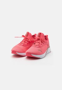 Par de zapatillas deportivas Puma de color coral rosa con tejido texturizado, cordones atados y suelas blancas sobre un fondo blanco.
