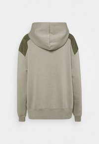 Sudadera color beige claro con un acabado texturizado. Presenta acentos en verde oliva en los hombros, una capucha con cordón y puños y dobladillo acanalados.