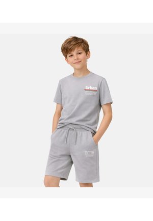 Jongen draagt een lichtgrijs T-shirt en bijpassende short met trekkoord en witte opdruk, staat met handen in de zakken tegen een effen achtergrond.