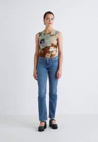 Telesna obleka v tie-dye slogu v zemeljskih tonih v kombinaciji z visokim pasom modrimi jeans hlačami s pravimi nogavicami in zelenimi platformnimi čevlji.