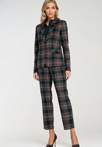 Brązowy i granatowy garnitur w kratę z dopasowaną marynarką i prostymi spodniami, charakteryzujący się gładką fakturą i klapami notch. Czubki butów dopełniają stylizację.