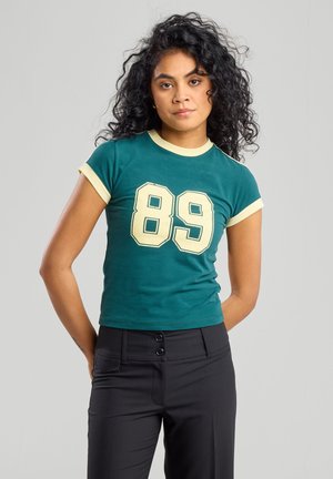 Camiseta de algodón verde con ribete amarillo y mangas cortas, que presenta un gran número "89" en bloque impreso en la parte delantera.