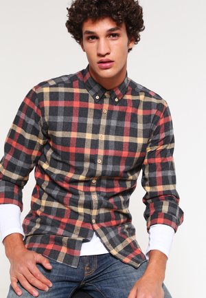 Zwarte, rode en gele geruite flanellen shirt met een button-down kraag en lange mouwen. Bevat knopen aan de voorkant en een wit onderhemd.